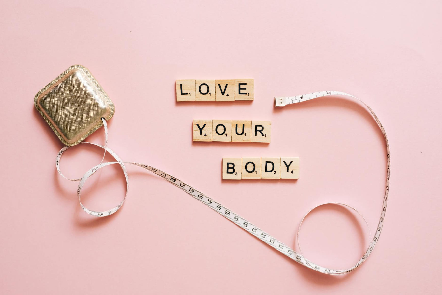Scrabble letters spelling 'Love Your Body' with a tape measure on a pink backdrop. on Think Lean Live Strong