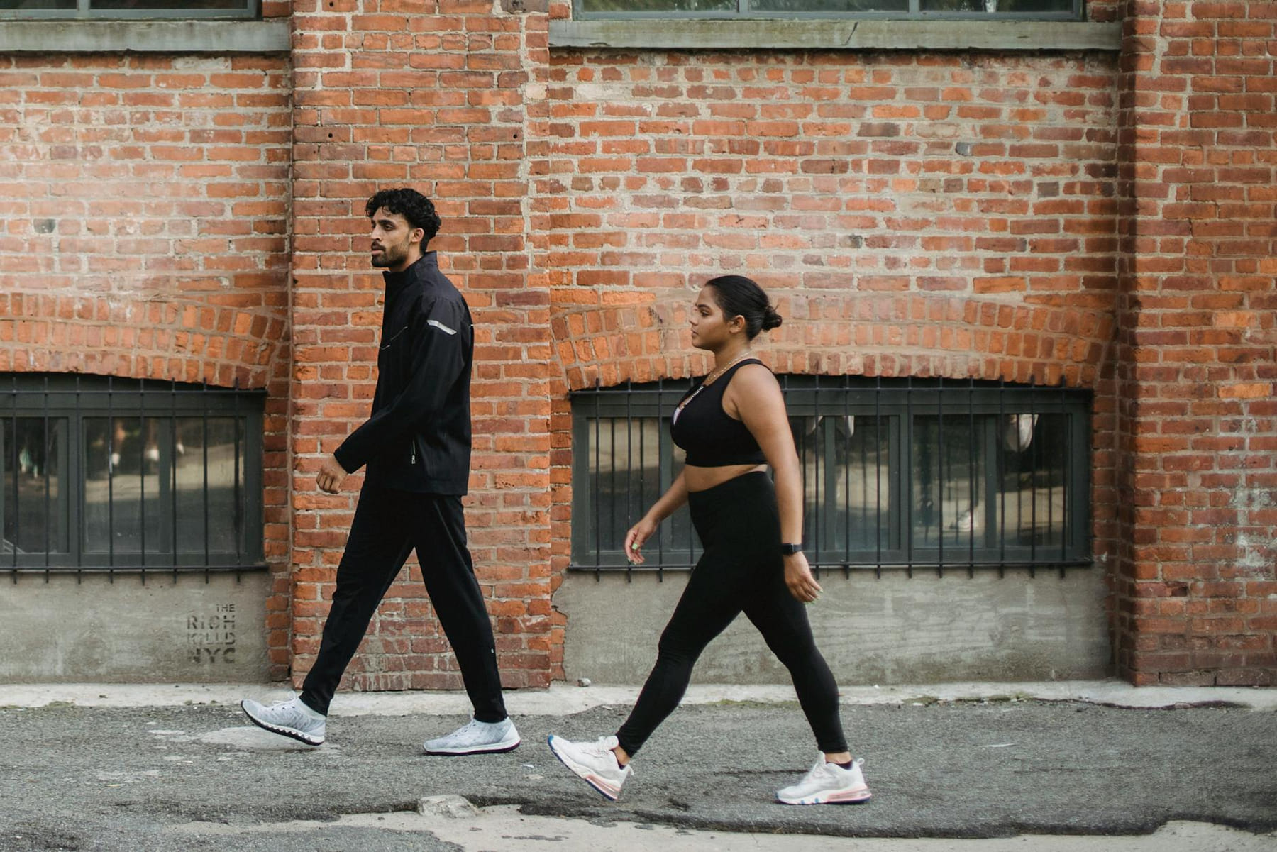 A man and woman walking briskly in sportswear against a brick wall in the city. on Think Lean Live Strong