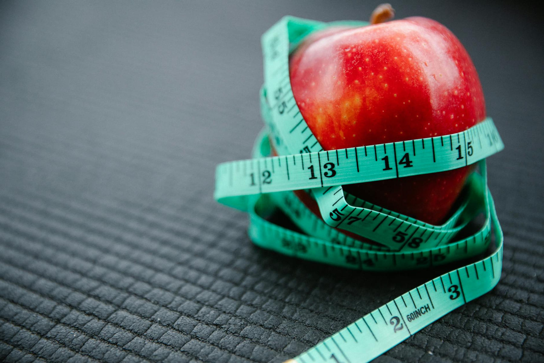 A vibrant red apple encircled by a blue measuring tape, symbolizing health and weight management. on Think Lean Live Strong