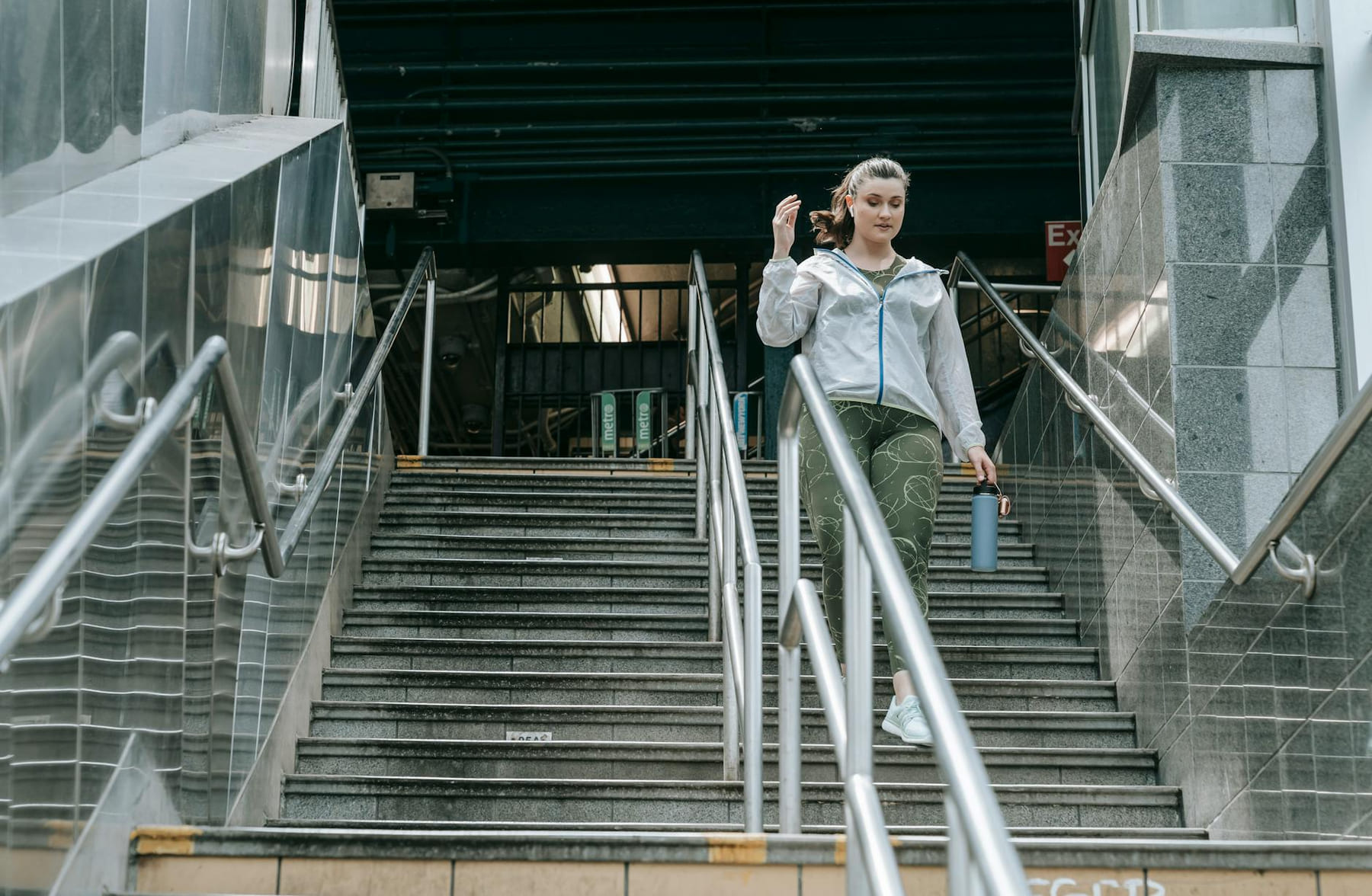 Woman in sportswear descending stairs, holding a water bottle, outdoors. on Think Lean Live Strong