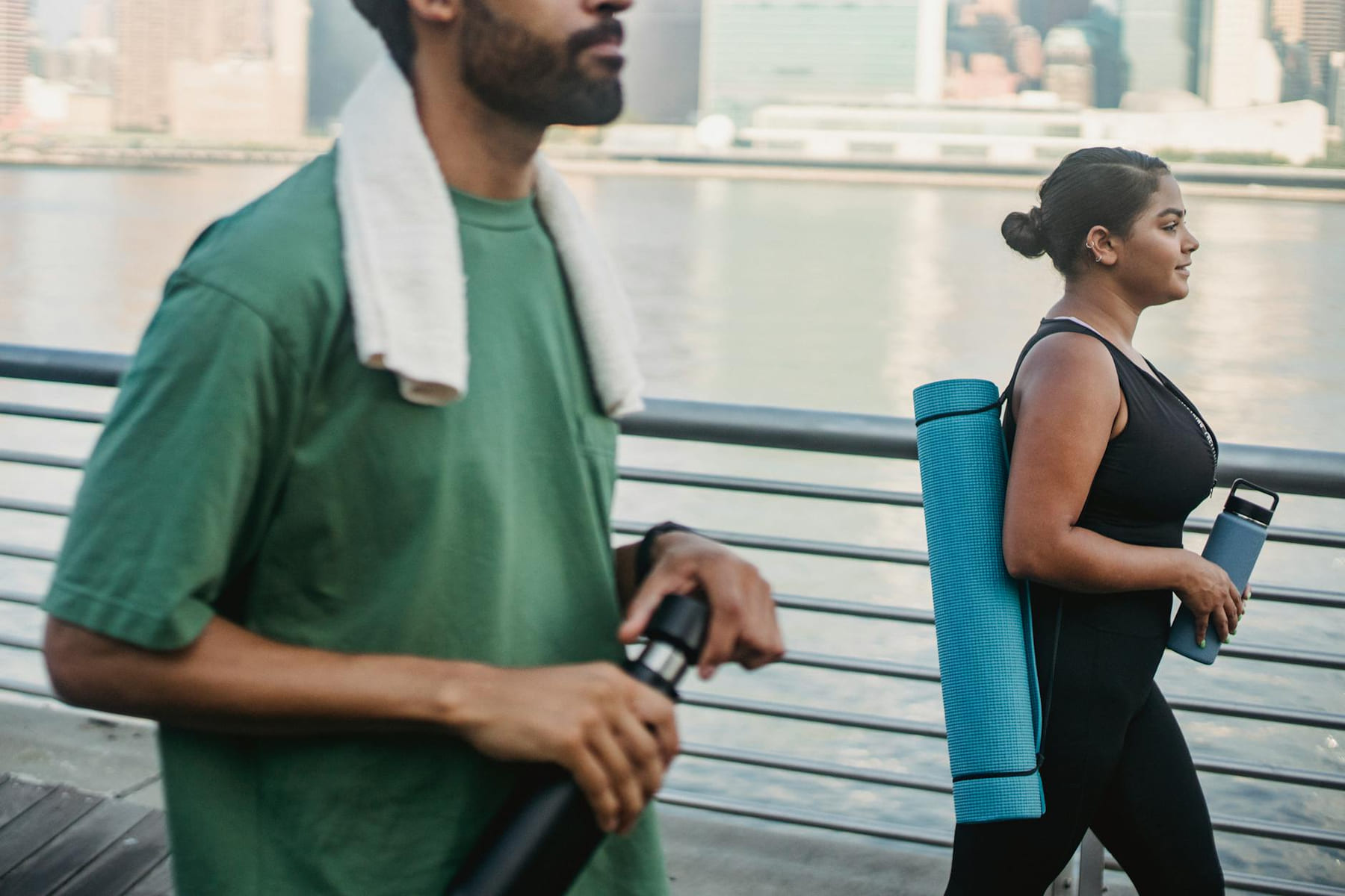 Two friends walking outdoors by the water, carrying yoga gear and bottles, embracing a healthy lifestyle. on Think Lean Live Strong