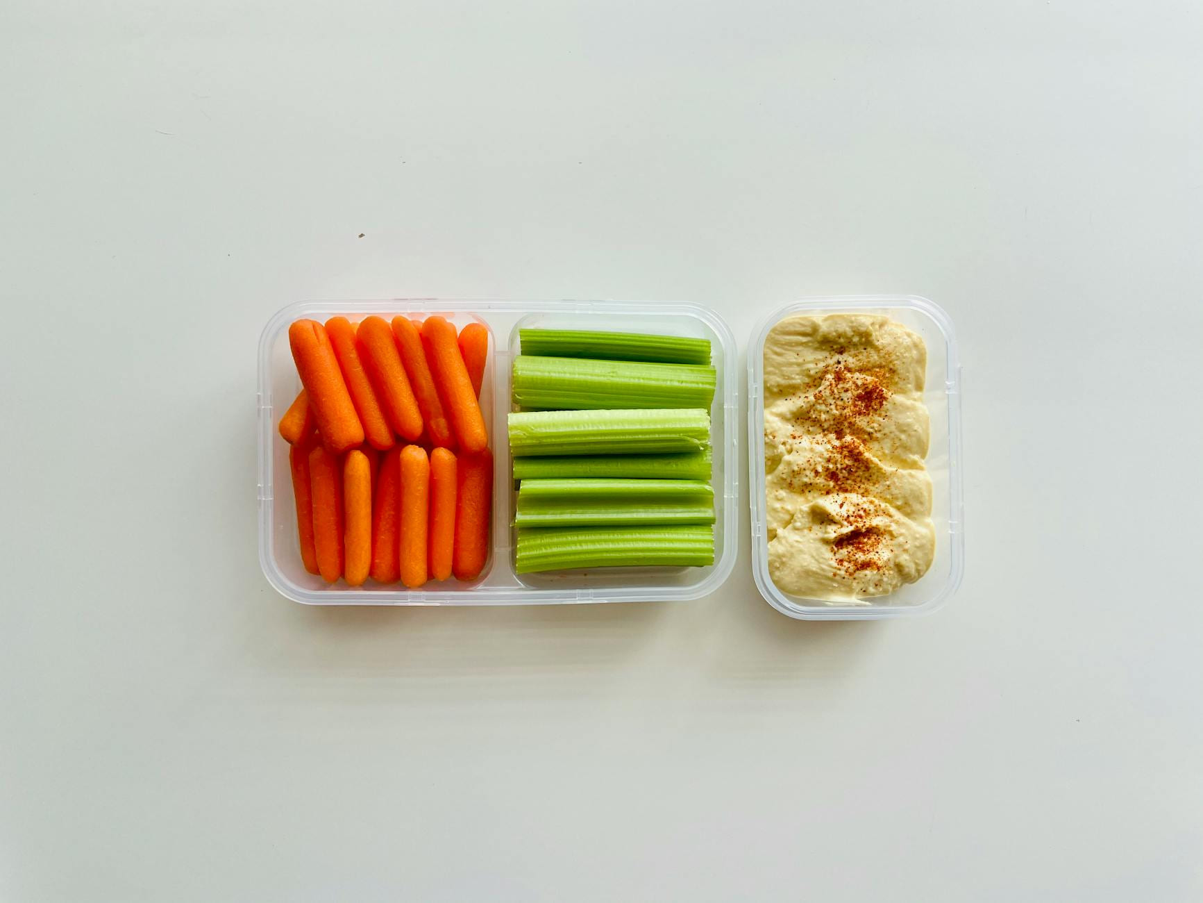 Fresh baby carrots, celery sticks, and hummus in a container for a healthy snack. on Think Lean Live Strong